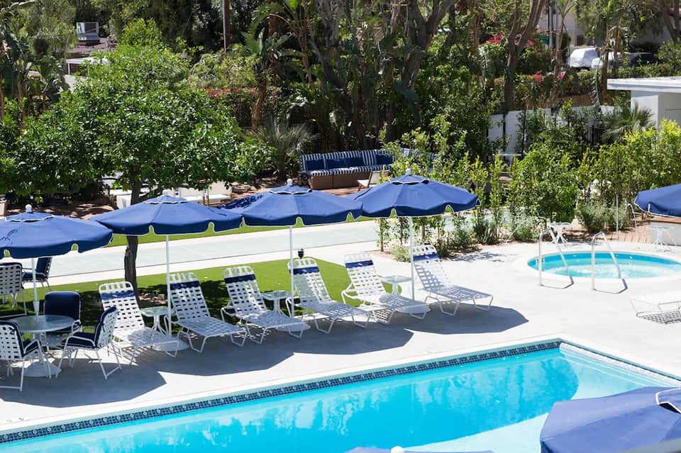 Pool area with blue umbrellas, lounge chairs, and landscaping