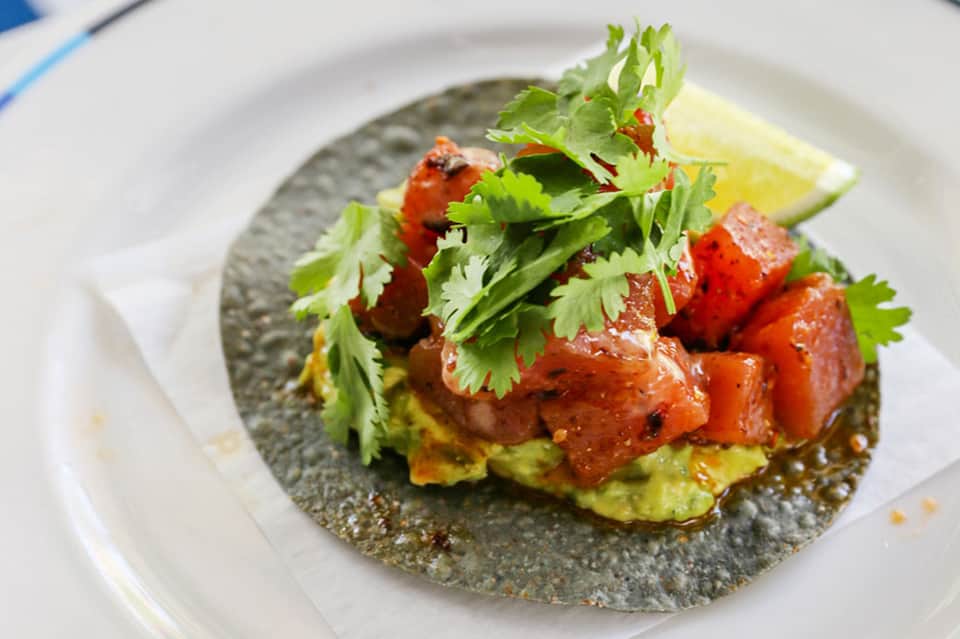 Gourmet tostada appetizer with avocado, tomato, cilantro on gray plate