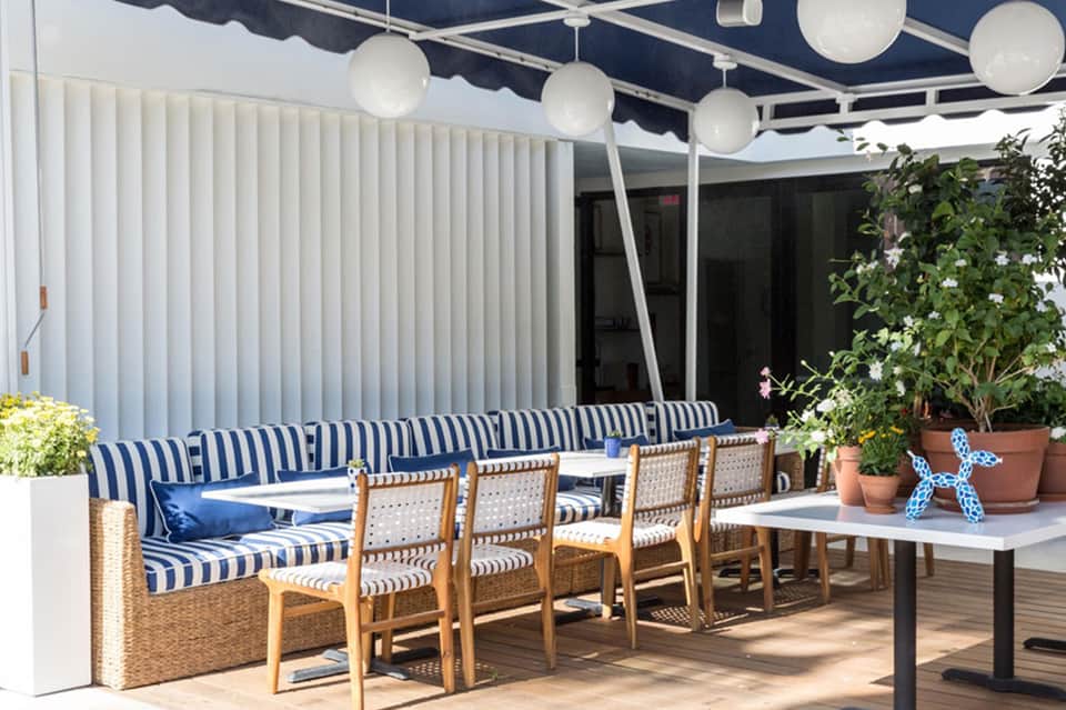 Contemporary terrace lounge with navy striped seating, pendant lighting, potted plants, and retractable shade
