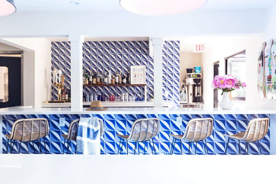 Contemporary bar with blue geometric tile pattern, white rattan stools, and shelved liquor display