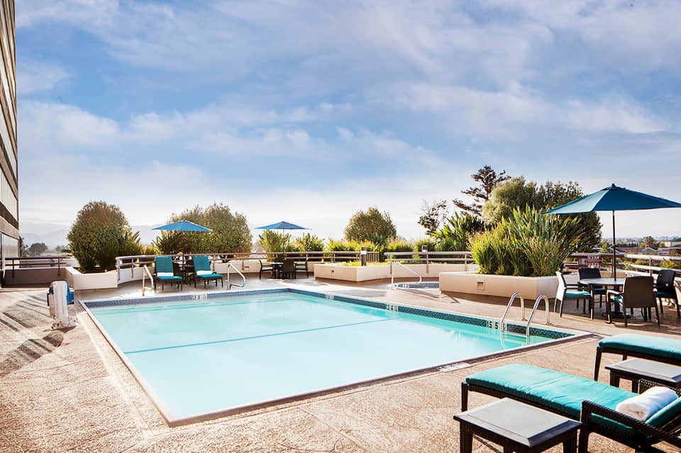 Rooftop pool with turquoise umbrellas, lounge chairs, landscaping, and city views