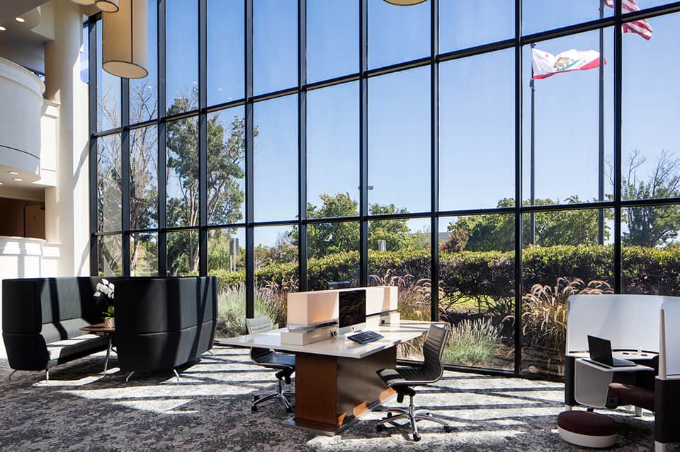 Modern office space with floor-to-ceiling windows, minimalist furniture, and green views