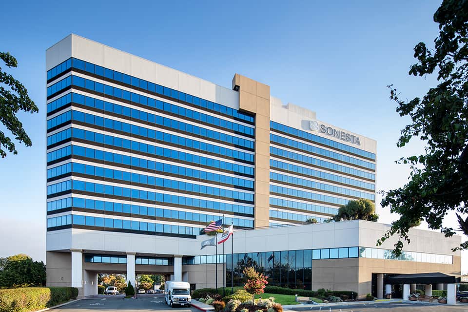 Modern glass and concrete hotel tower with blue-tinted windows and ground-level entrance portico