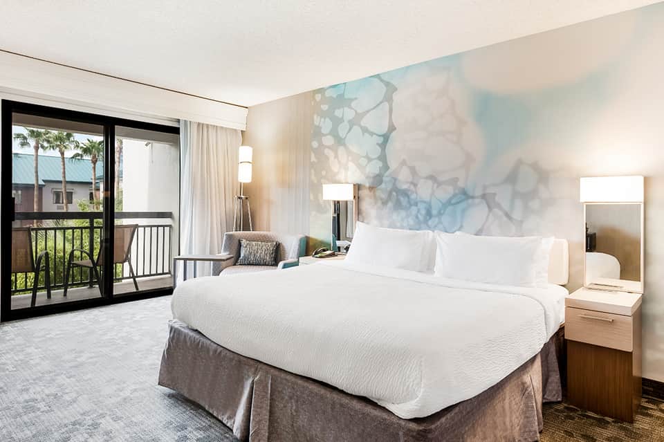 Modern hotel bedroom with king bed, balcony, and abstract headboard art