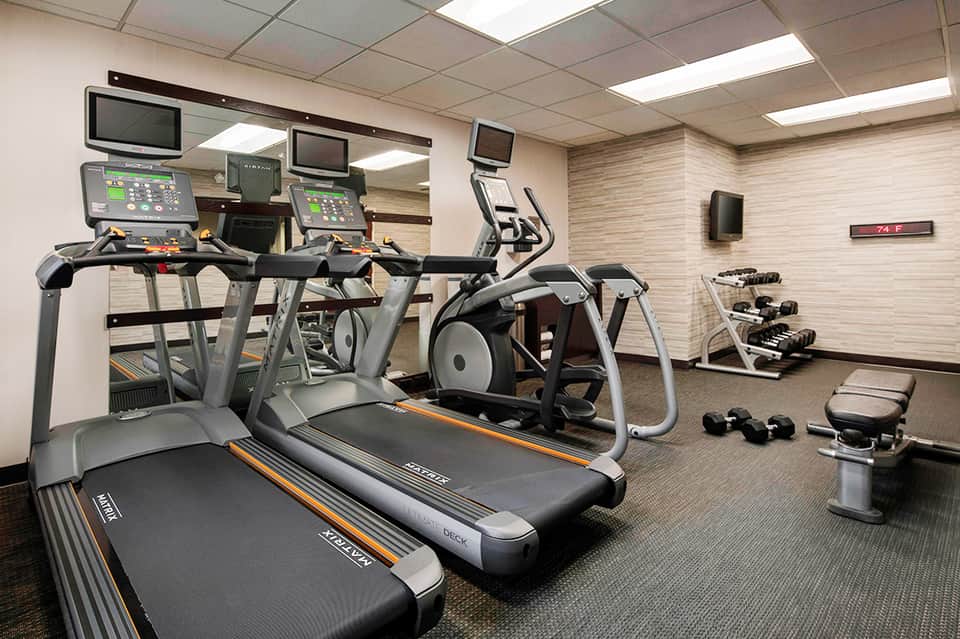 Modern fitness center with treadmills, exercise bikes, dumbbells, monitors, and wood-textured walls