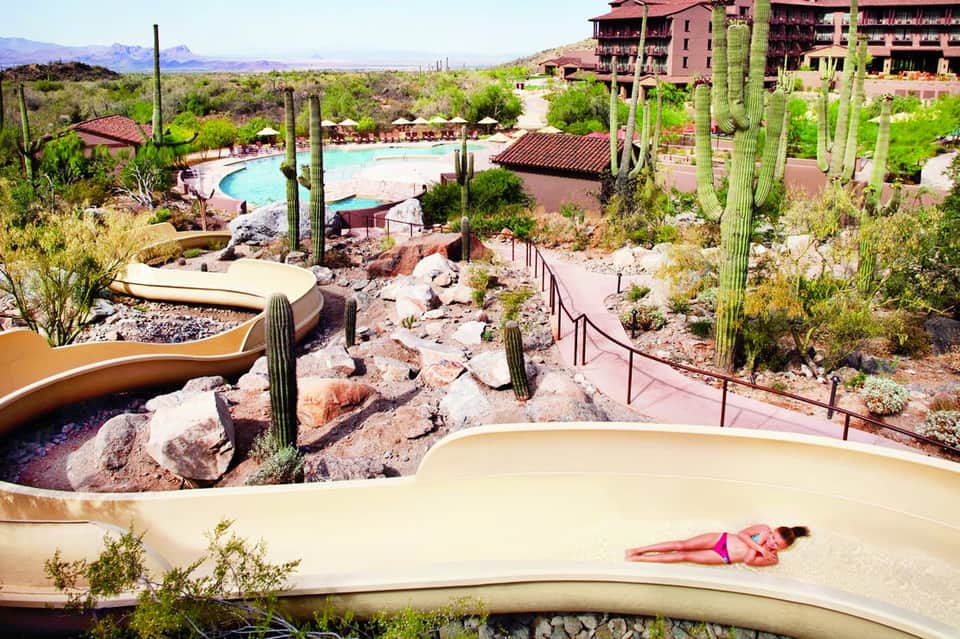 Desert resort with curved sand lazy river, saguaro cacti, and guest in pink bikini
