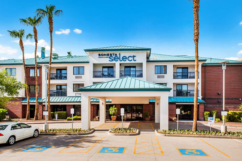 Sonesta Select hotel exterior with brick facade, turquoise metal roof, and palm landscaping