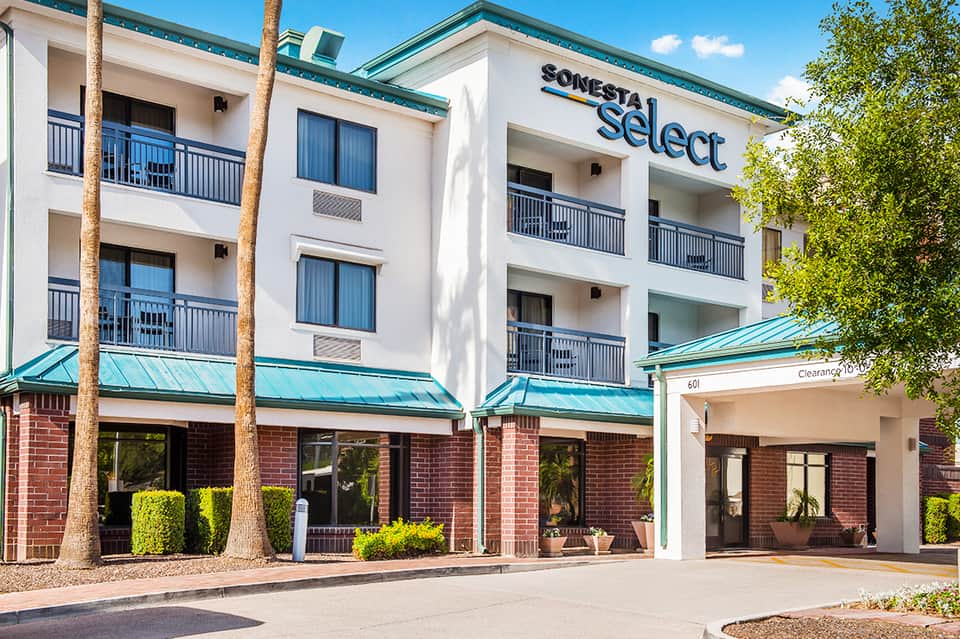 Sonesta Select hotel exterior with turquoise trim, three-story white and brick facade, and ground-level retail
