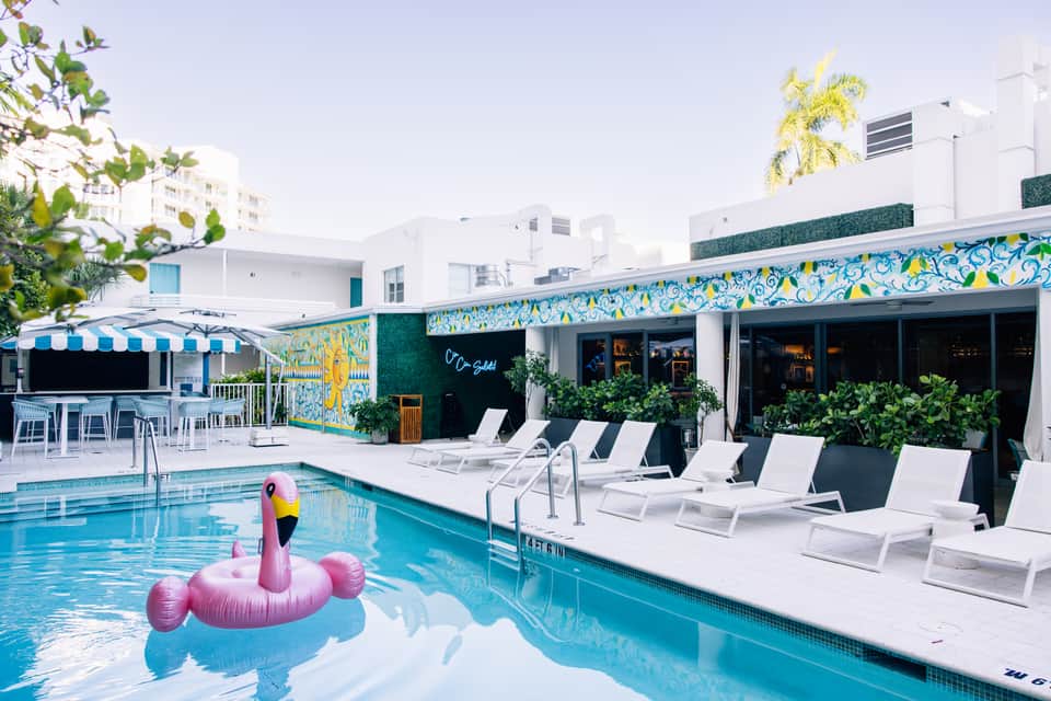 Modern pool with pink flamingo float, colorful accent wall, and white lounge chairs
