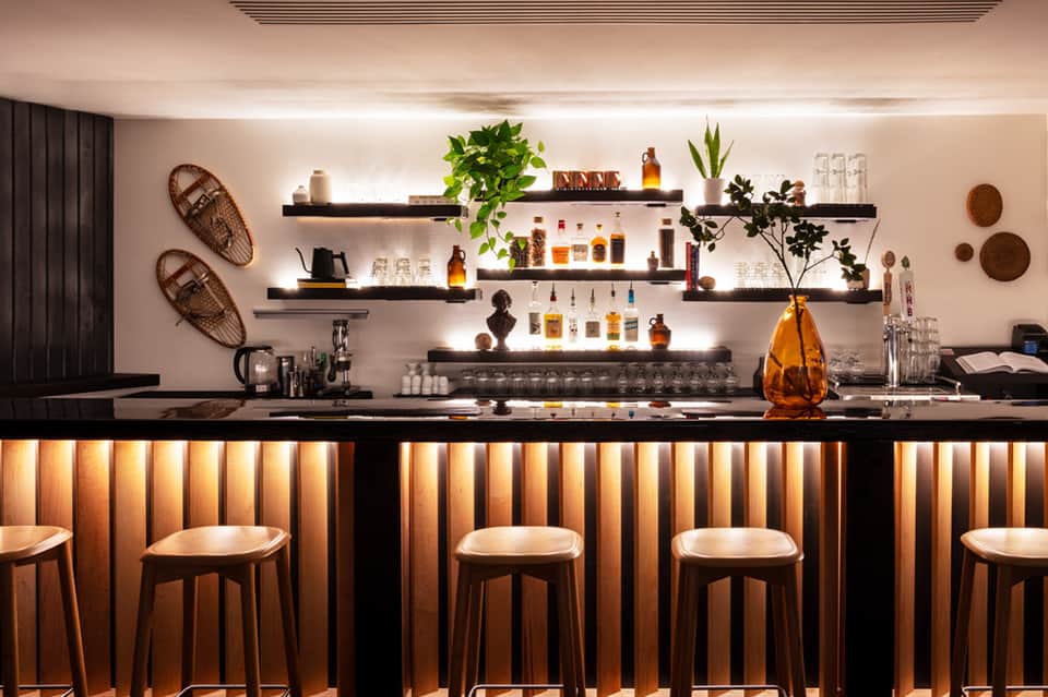 Modern spa bar with black counter, wooden stools, and illuminated shelving display