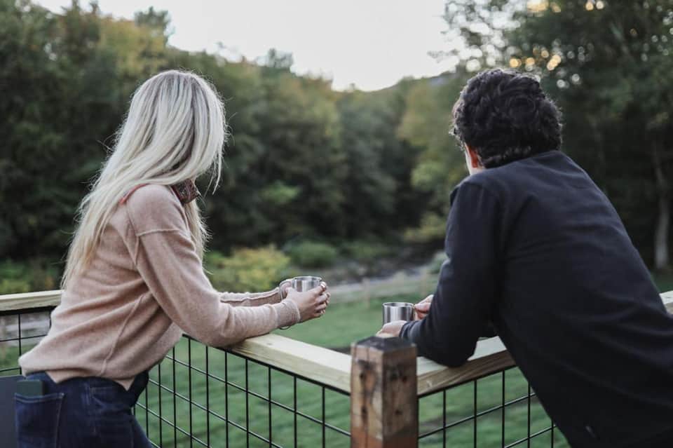 Two people enjoying drinks on a scenic overlook with forested landscape