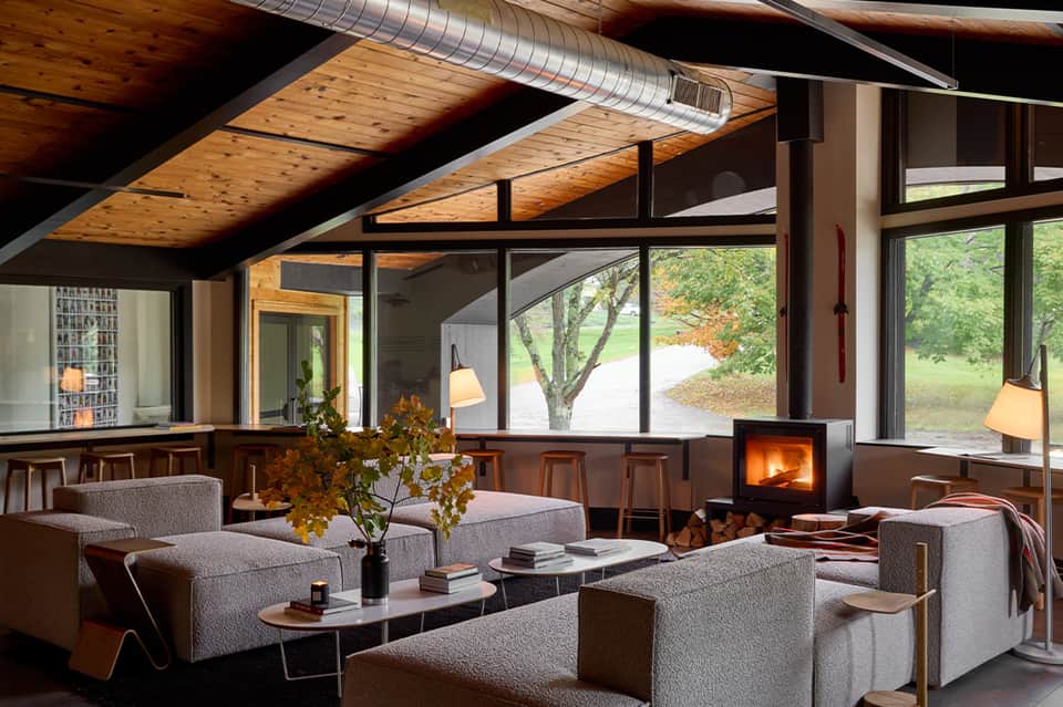 Contemporary resort lounge with fireplace, wooden beams, gray seating, and floor-to-ceiling windows