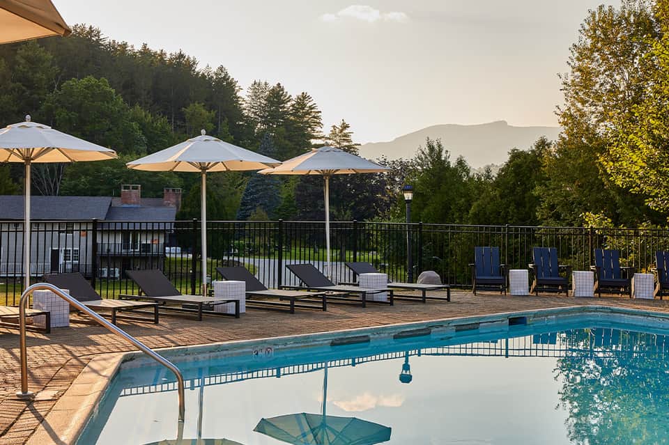 Resort pool deck with blue water, lounge chairs, white umbrellas, mountains visible in background