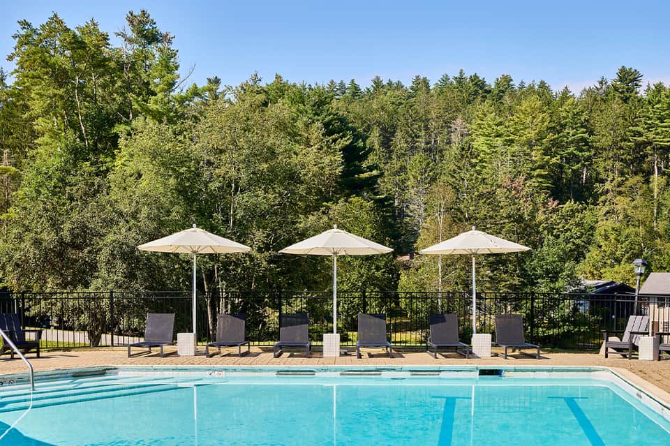 Olympic-style lap pool with three white umbrellas and forest backdrop in daylight