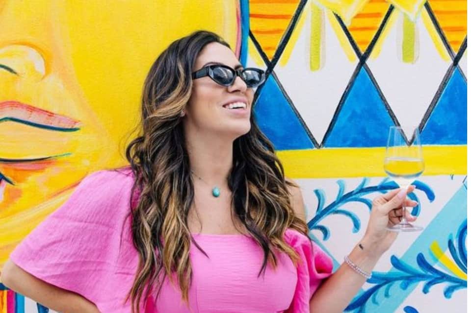 Woman in pink outfit and sunglasses posing against colorful geometric mural backdrop