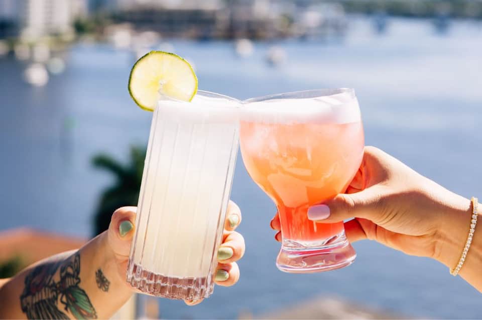 Two people toasting with tropical cocktails overlooking the waterfront