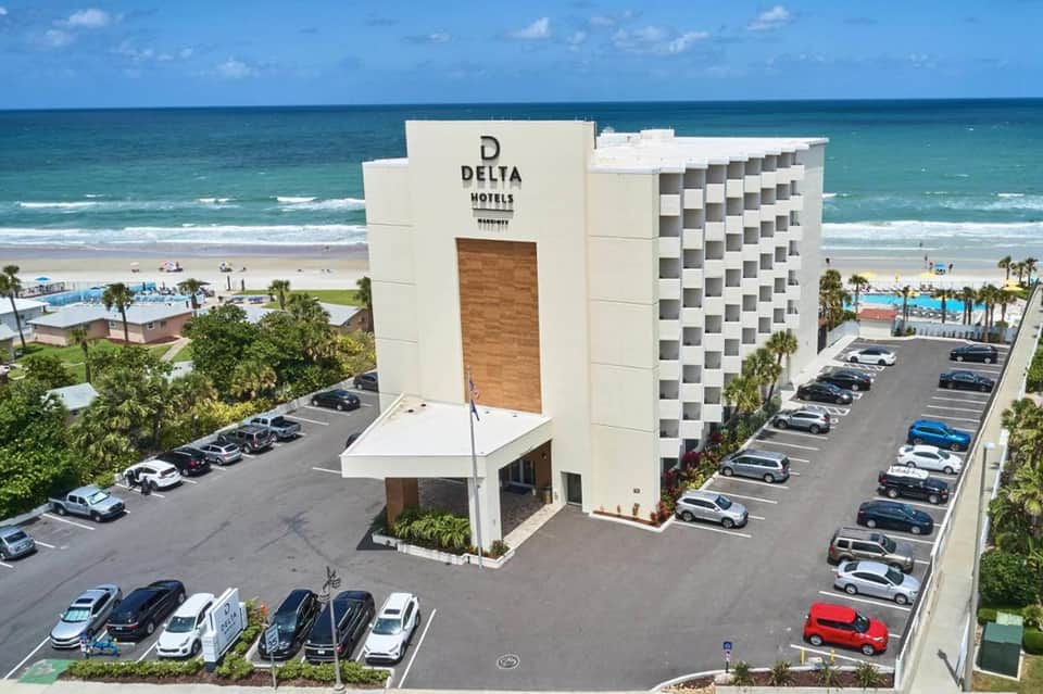 Aerial view of Delta Hotels beachfront property with modern white building, pool, beach, and parking lot