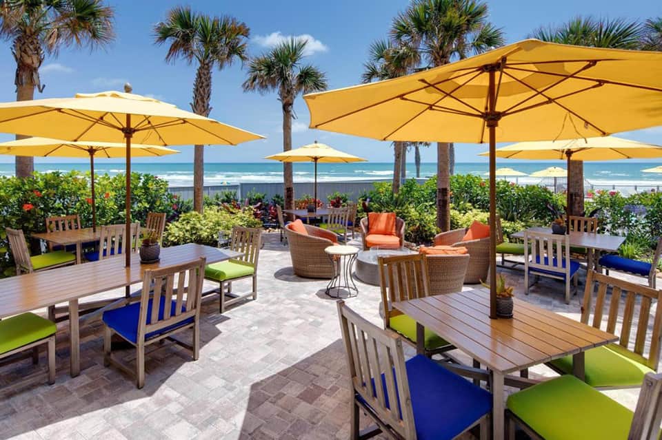 Beachfront dining area with yellow umbrellas, wooden tables, and ocean view