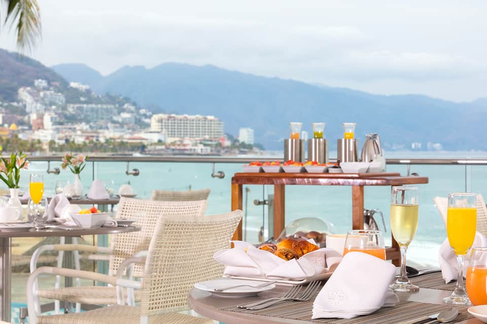 Beachfront breakfast terrace with ocean and mountain views, cocktails, and wicker seating