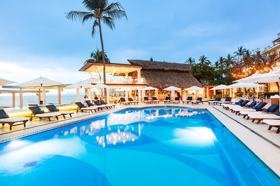 Luxury beachfront resort pool at sunset with palm trees and ocean views