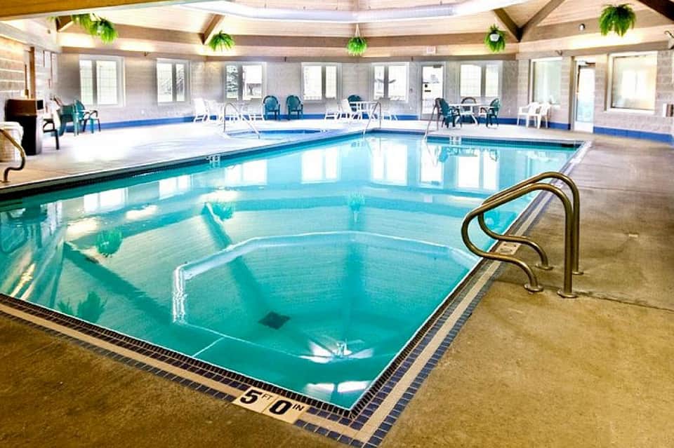 Indoor heated pool facility with skylights, lounge seating, and spa hot tub in spacious hall