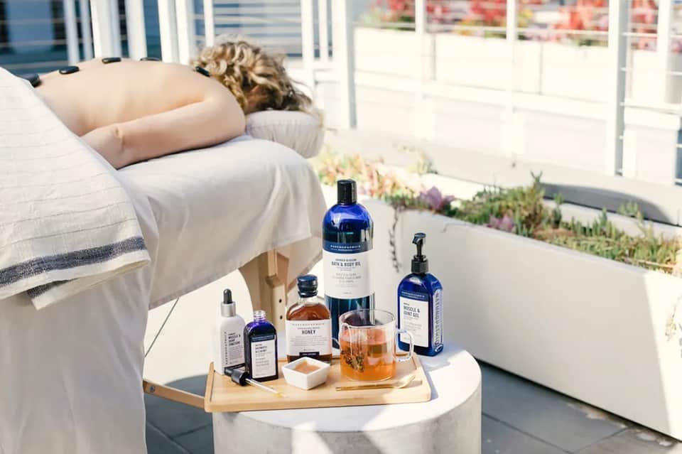 Spa products and honey on table next to person relaxing on lounge chair by pool
