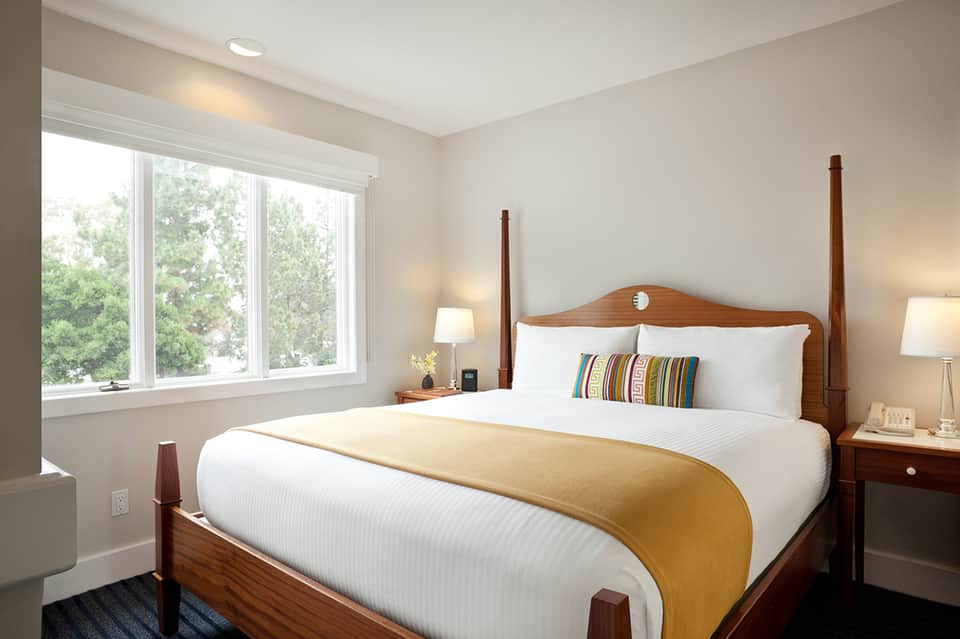 Bright bedroom with queen bed, wood headboard, large windows overlooking trees, and warm neutral tones