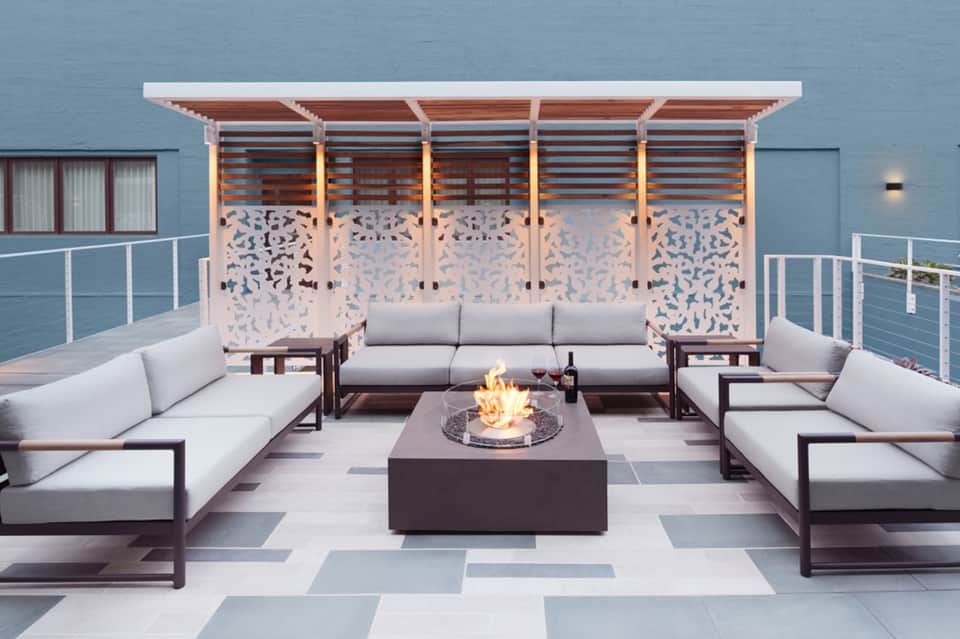 Rooftop lounge with modern seating, fire pit, decorative panels, and ocean-blue wall backdrop