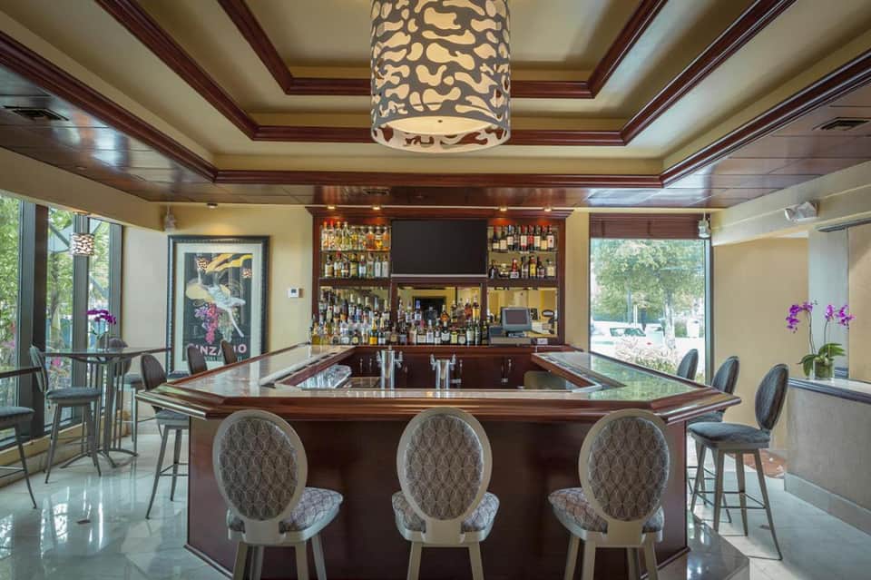 Elegant resort bar lounge with wooden coffered ceiling, stocked liquor shelves, and patterned pendant light