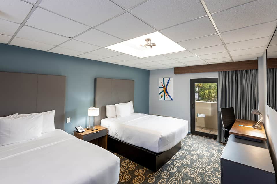 Hotel room with two queen beds, blue walls, desk area, and sliding glass door