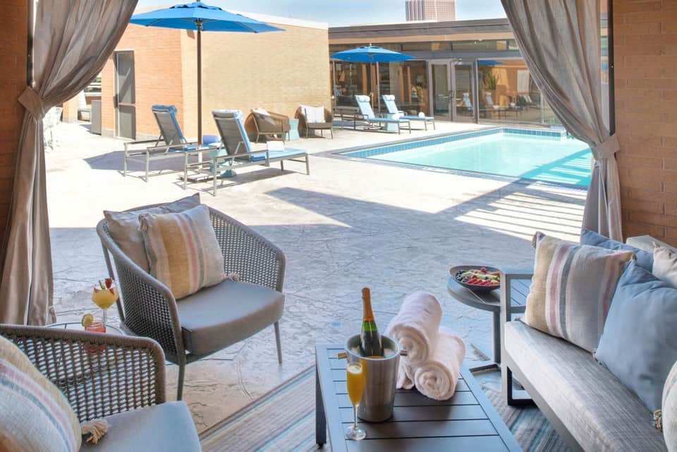 Rooftop pool lounge with gray curtains, cushioned seating, champagne bucket, pool view, and modern architecture
