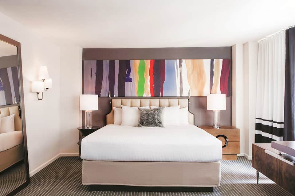 Hotel bedroom with beige upholstered headboard, colorful abstract art, and modern furnishings