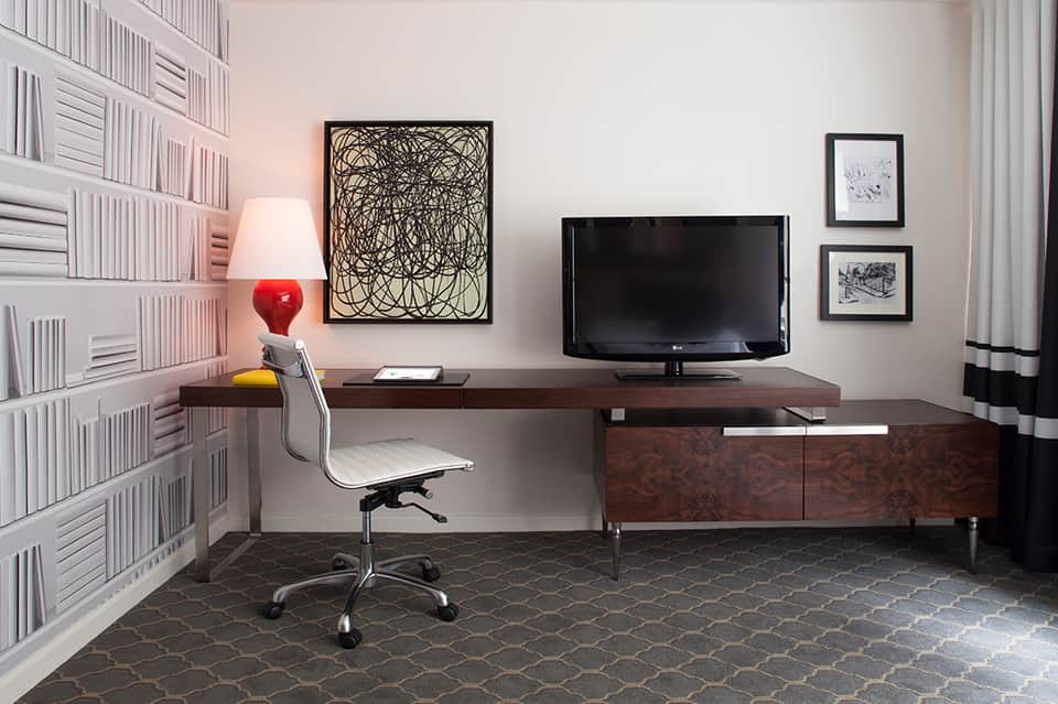 Home office with dark desk, TV, bookshelf, and red desk lamp