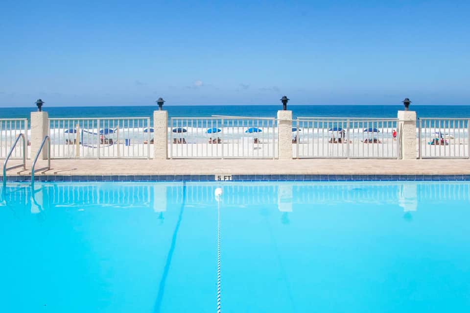 Olympic-length swimming pool with lane dividers overlooking the ocean and beach with umbrellas