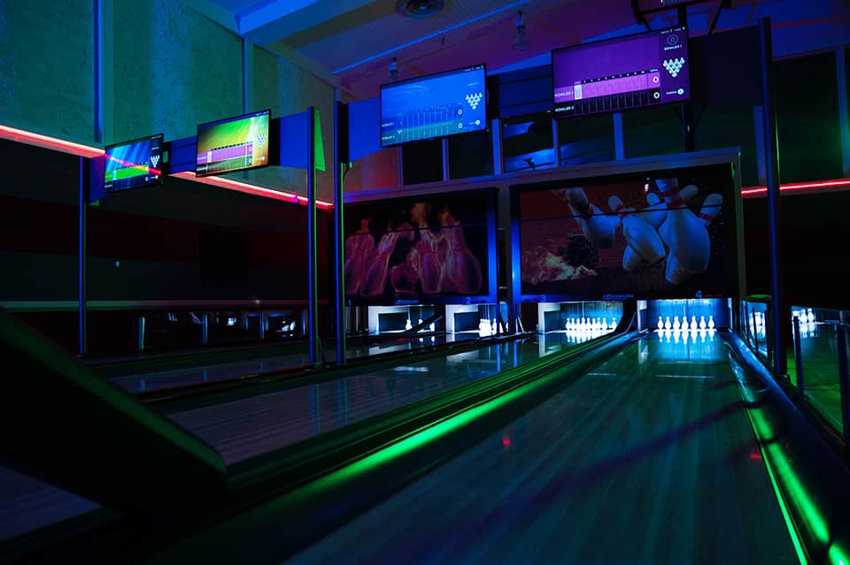 Modern bowling alley with neon green and pink lighting and video screens overhead