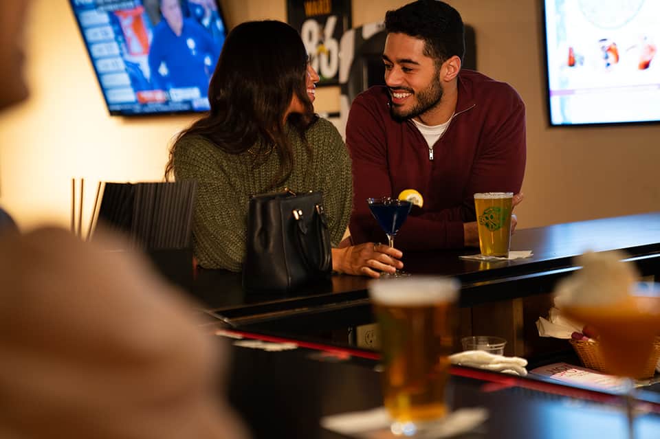 Couple enjoying drinks at bar counter with sports displays and casual indoor resort atmosphere
