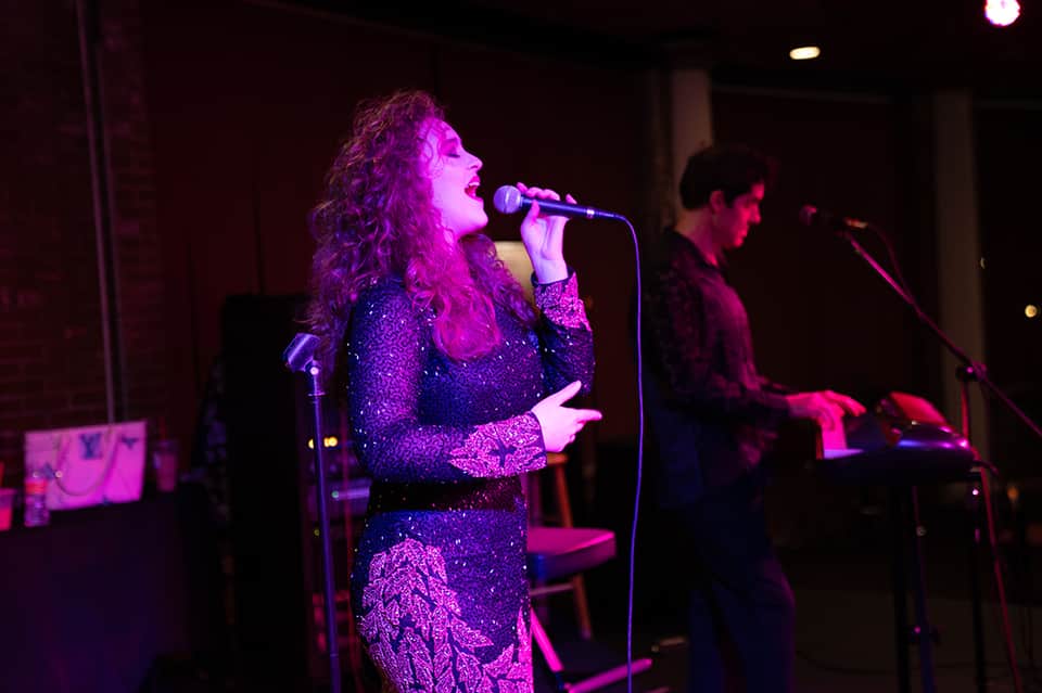 Female performer on stage singing into microphone with purple stage lighting