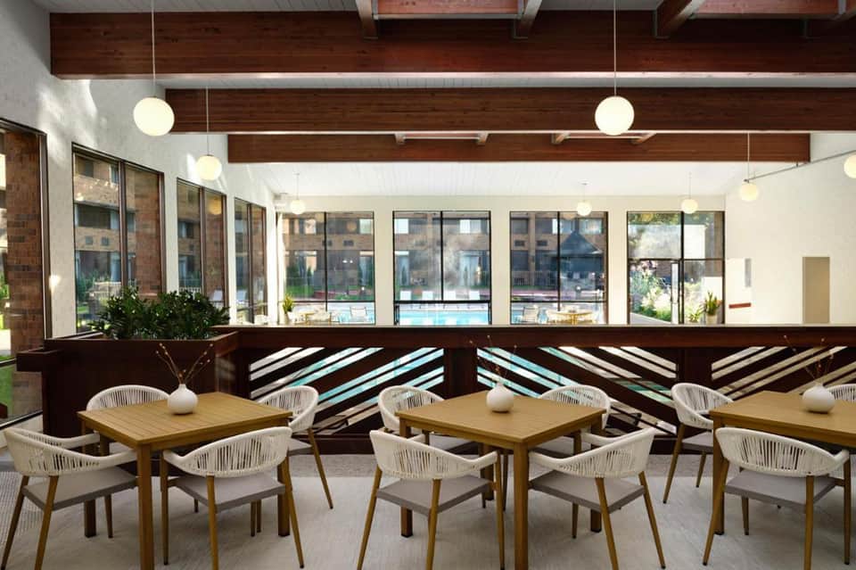 Contemporary pool-view café with wooden tables, white chairs, and large windows