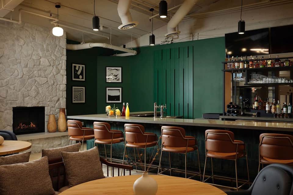 Modern hotel bar with green walls, fireplace, leather seating, and illuminated bar counter
