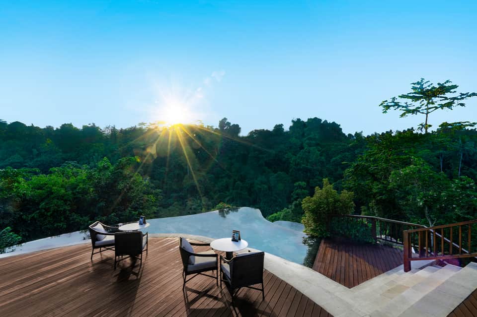 Infinity pool overlooking jungle landscape at sunrise with mountains