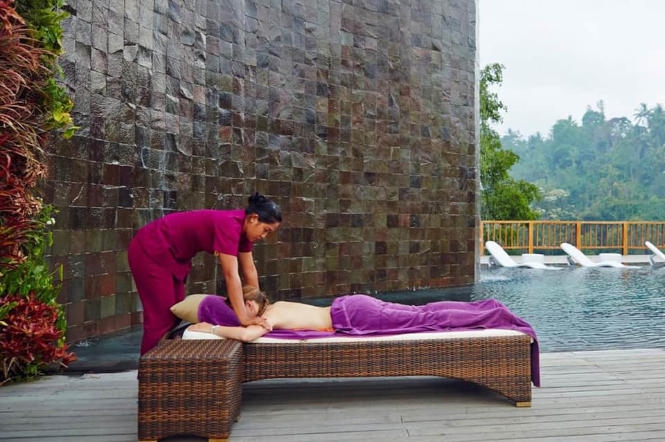 Spa therapist providing massage treatment on outdoor platform overlooking mountain scenery