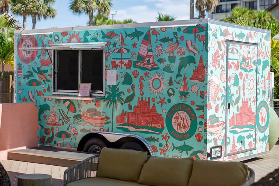 Colorful food truck with turquoise and coral beach-themed artwork and serving window.