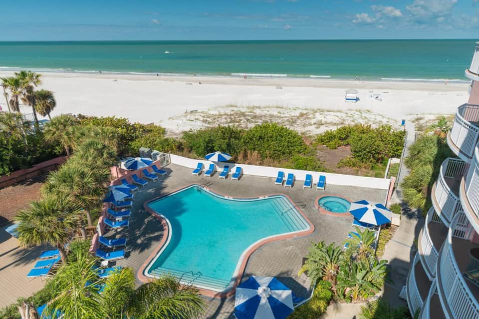 Beachfront resort pool with turquoise water, blue lounge chairs, ocean view, and palm trees