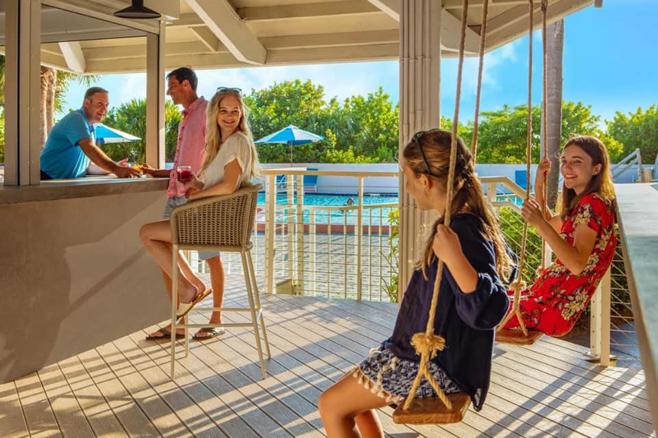 Family enjoying waterfront bar area with pool view and palm tree landscape