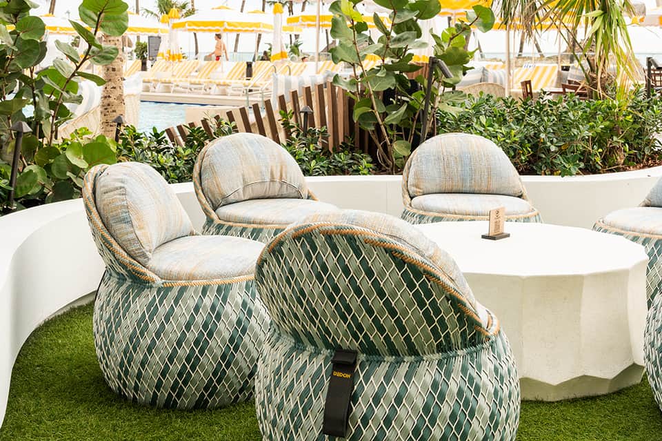 Luxury poolside lounge with woven basket chairs, white tables, grass area, and yellow umbrellas