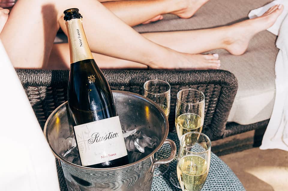 Champagne bottle in ice bucket with filled glasses on textured sofa fabric