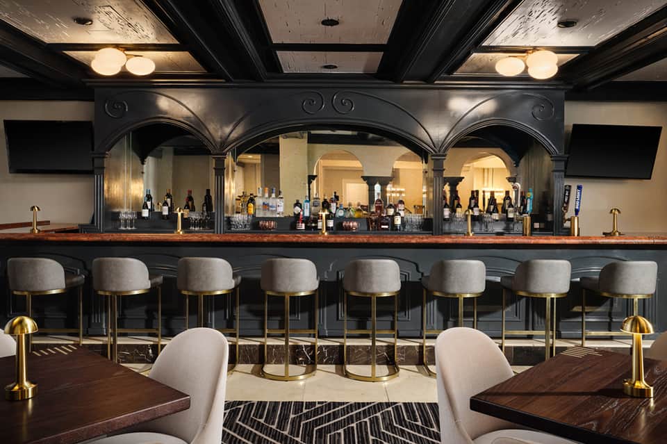 Elegant bar with dark finish, brass accents, upholstered seating, and full liquor selection