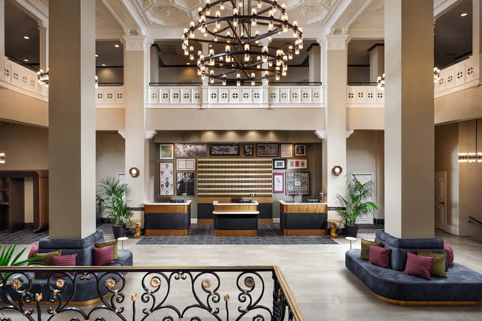 Grand hotel lobby with double-sided chandelier, reception desks, white columns, and elegant decor