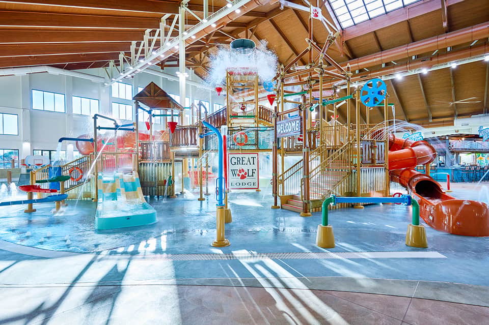 Indoor water park with slides, splash area, and colorful play structures under skylights