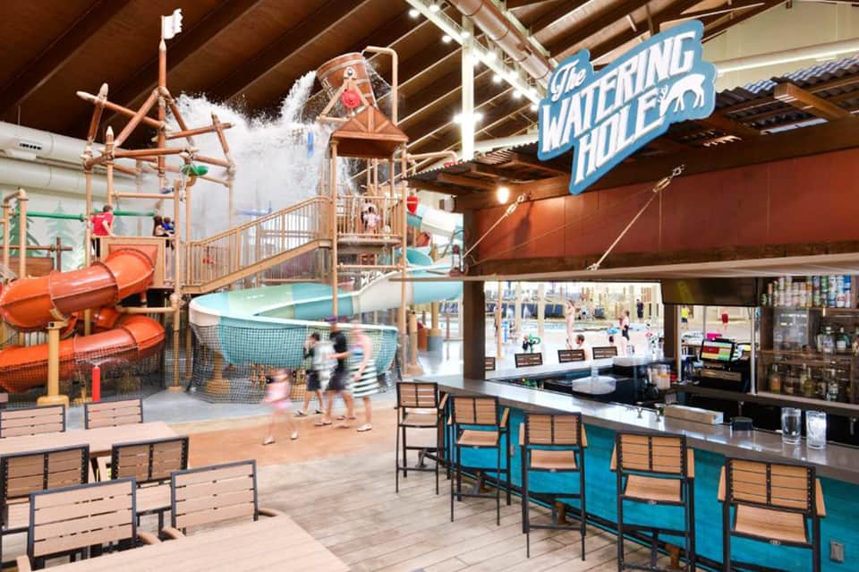 Indoor water park with orange slide tower, splash pool, and watering hole play structure